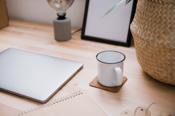 Laptop and cup of coffee placed on wooden table with green houseplant in bright home office