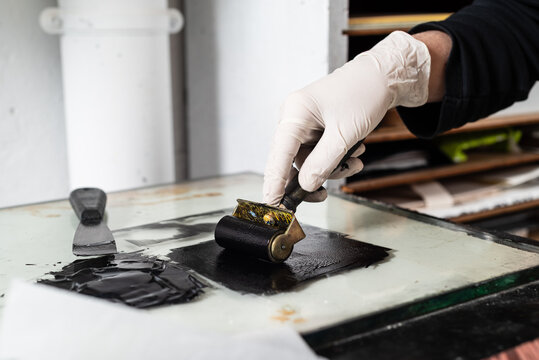 Closeup hand of crop anonymous artisan in glove using braver and spreading ink on sheet for engraving while working in professional workshop
