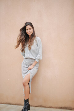 Charming female with long hair and in casual dress standing near building on street and modestly looking at camera