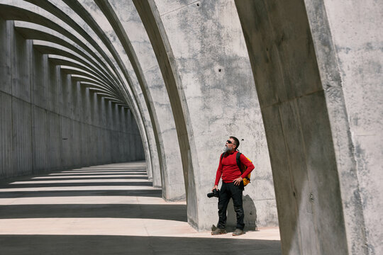 Traveling male photographer with professional photo camera taking picture of amazing arched passage in city on sunny day