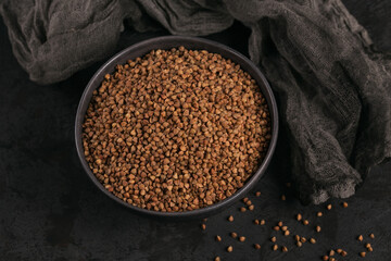 Bowl of dry raw buckwheat groats on a dark background. Cooking buckwheat porridge concept.