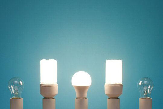 bulb, compact fluorescent lamp, LED lamp in one line on a blue background. LED lamp and compact fluorescent lamp are on.