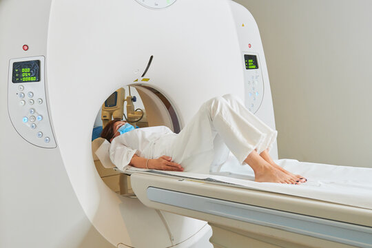 Barefoot patient in white wear lying with closed eyes on couch of tomography machine in hospital