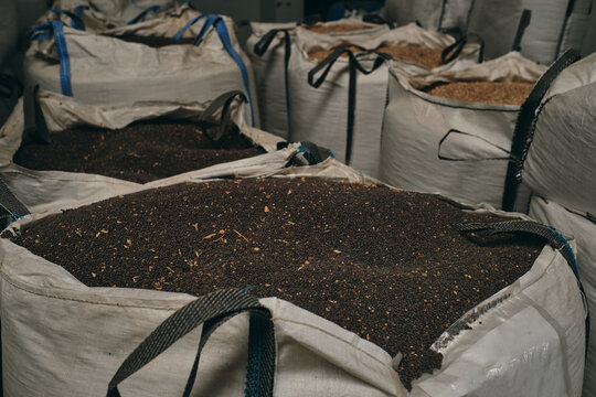 Huge bags with black grain crops stored in stock in industrial facility of factory