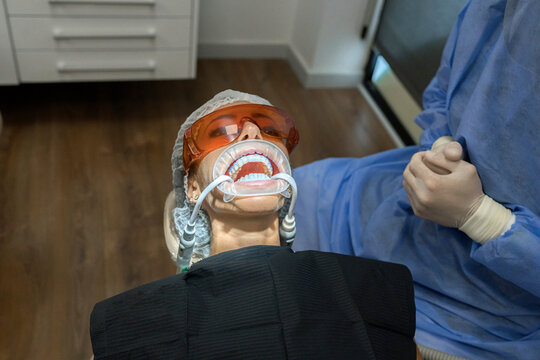 From above cropped unrecognizable professional stomatologist sitting near patient with expander in mouth in modern clinic