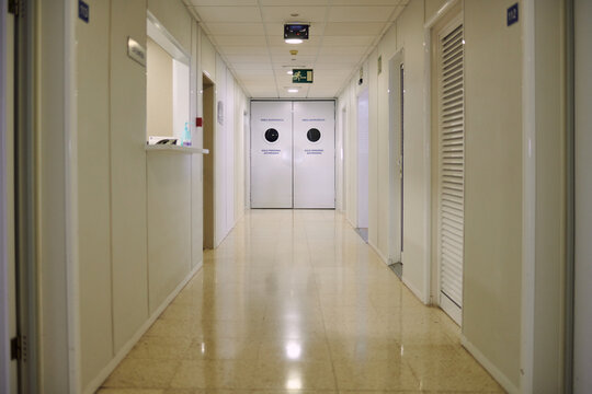 Doors in empty passage with glowing tiled floor illuminated by lamps in modern clinic