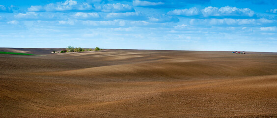 panoramic view of fields prepared for sowing, smooth lines on hilly terrain in spring with cloudy sky