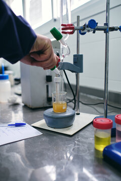Hand of unrecognizable male chemist pouring liquid into flask while performing chemical experiment in laboratory
