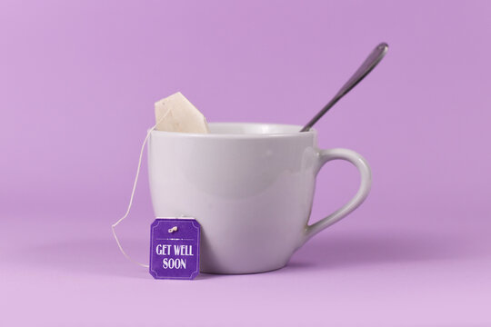 Tea bag with made up label with text 'Get well soon' in tea cup on violet background