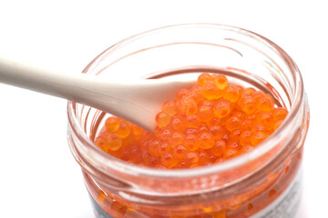Closeup of trout eggs in a glass container with a ceramic spoon on white background