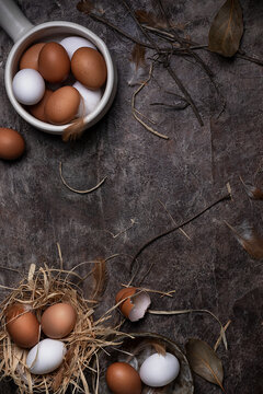 Top view of cracked and whole chicken eggs of white and brown colors arranged on messy surface with feathers