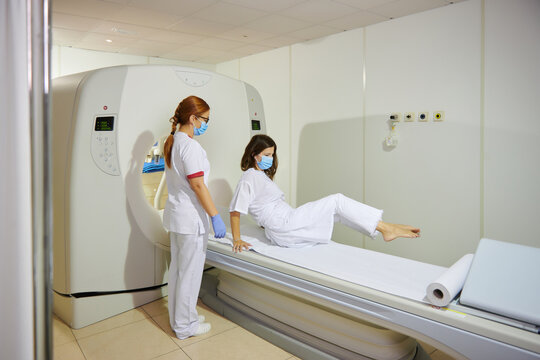 Doctor in uniform and eyeglasses using tomography machine with lying female patient in hospital