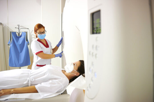 Anonymous doctor in uniform and eyeglasses using tomography machine with lying female patient in hospital