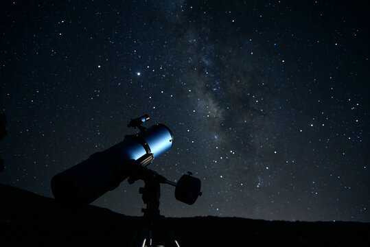 Modern optical telescope against cloudless dark sky with glowing stars at night time