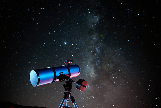 Modern optical telescope against cloudless dark sky with glowing stars at night time