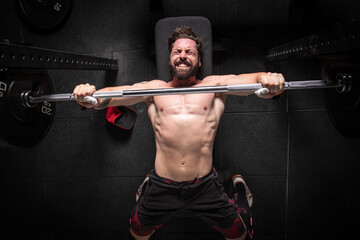 From above of strong male athlete lying on bench press and doing exercises with heavy barbell during workout in gym
