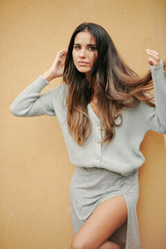 Charming female with long hair and in casual dress standing near building on street and modestly looking away