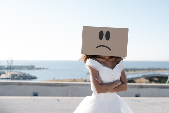 Unrecognizable woman wearing white bridal dress and carton box with sad face on sunny rooftop