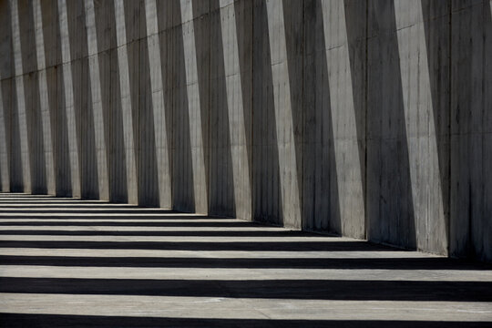 Columns of empty concrete walkway illuminated by sunlight casting lines of shadow on stone wall