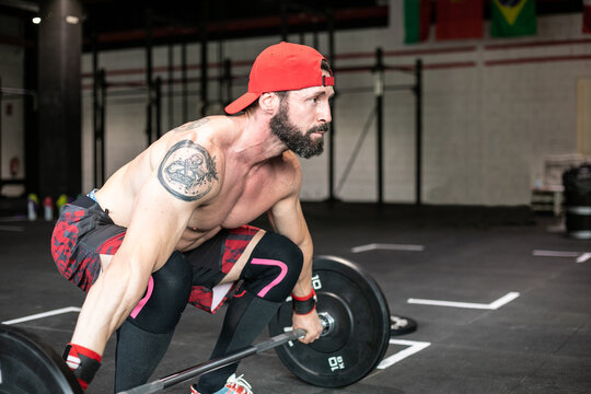 Side view of muscular focused shirtless male athlete doing clean and jerk exercise with barbell during weightlifting training in gym