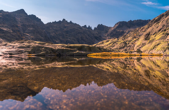 Picturesque view of pond with transparent water reflecting mountains under blue cloudy sky in Sierra de Gredos