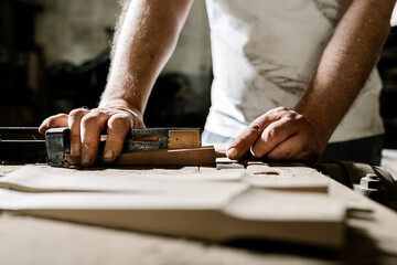 Crop male woodworker standing at old workbench and working with lumber details in grungy workshop