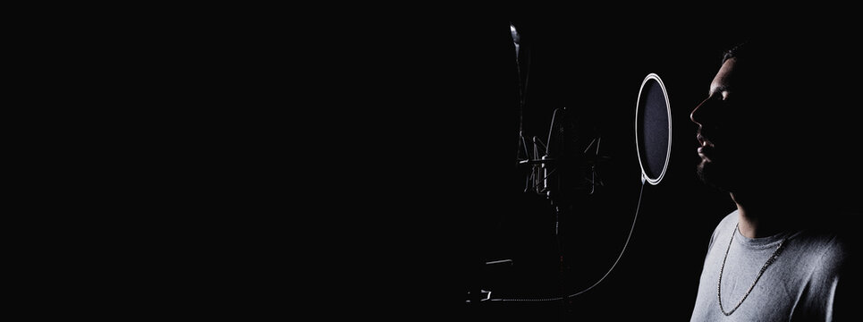 Side view of anonymous male singer in headphones standing in acoustic room with soundproof walls and microphone and recording song in studio