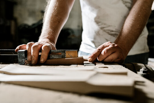 Crop male woodworker standing at old workbench and working with lumber details in grungy workshop