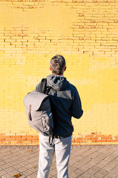 Retired senior man athlete looking at a yellow wall with sportswear and backpack
