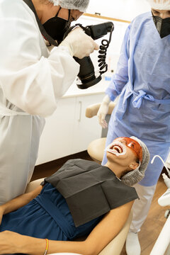 Professional dentist using portable X ray device for examining teeth of patient in protective goggles while working in modern dental clinic with assistant