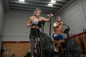 From below of cheerful sportswoman and sportsman cycling on stationary air bikes during active training in modern gym