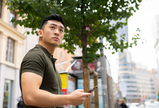 Side view low angle of serious Asian male browsing cellphone in city and looking away