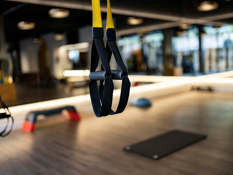 Elastic TRX ropes hanging on blurred background of contemporary gym during fitness workout