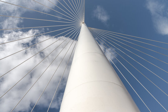 From below of white contemporary suspension bridge with high column connecting many cables together against blue sky