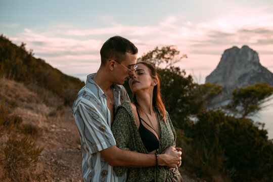 Side view of passionate couple hugging and kissing while standing on hill on background of sunset over sea