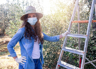 Portrait of young female farmer in protective mask looking at camera and resting after harvesting in field