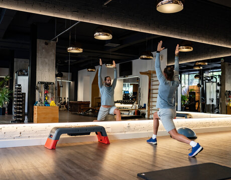 Back view of fit man doing lunges exercise during warm up session in modern gym
