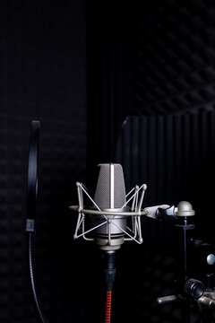 Contemporary metal microphone with wire placed on background of soundproof foam with pyramid shaped pattern in dark music recording studio