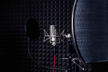 Contemporary metal microphone with wire placed on background of soundproof foam with pyramid shaped pattern in dark music recording studio