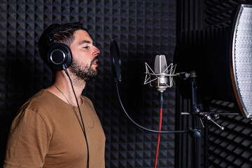 Side view of male singer in headphones standing in acoustic room with soundproof walls and microphone and recording song in studio