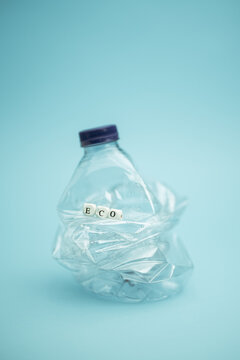 Crumpled plastic bottle placed on blue background in studio demonstrating concept of waste recycling