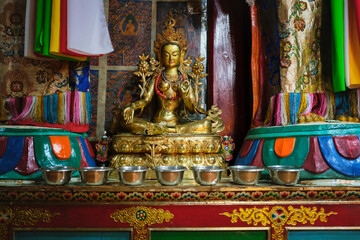 Interior of traditional oriental temple with golden figure of praying Buddha with metal bowls
