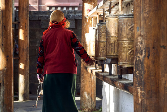 Back view of anonymous woman in stylish clothes turning Buddhist golden prayer wheels located in Sichuan
