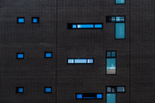 Abstract background of detail of modern building with dark wall with windows of different shapes and sizes