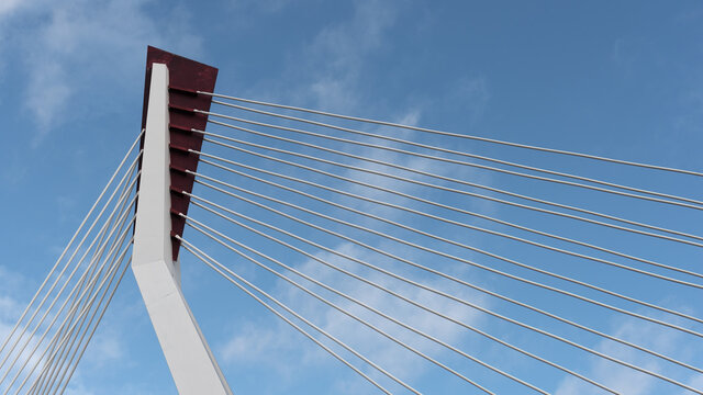From below of white contemporary suspension bridge with high column connecting many cables together against blue sky