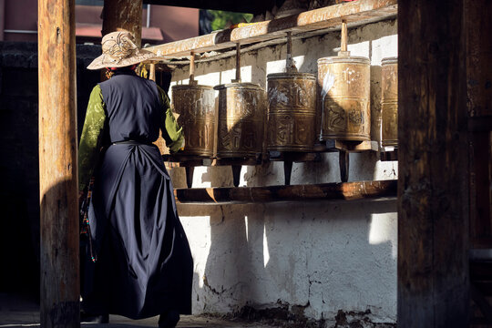 Back view of anonymous woman in stylish clothes turning Buddhist golden prayer wheels located in Sichuan
