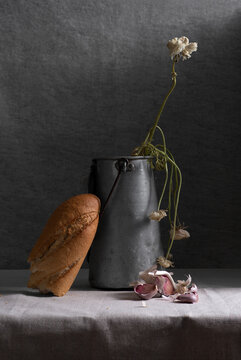 Rustic composition of metal jar with weathered flowers and piece of white bread on table