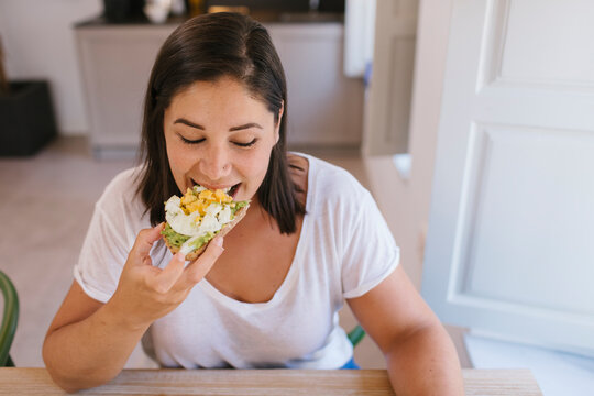 Woman biting a breakfast toast of avocados and eggs