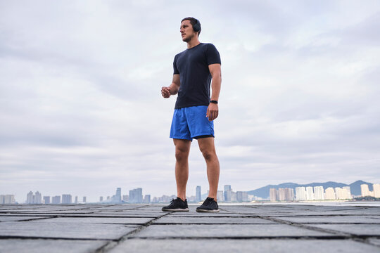 Ground level of determined male athlete in wireless headphones listening to music during workout while standing and looking away