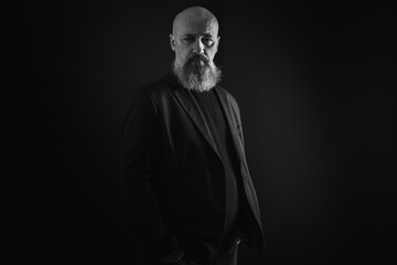 Obraz premium close up photo, portrait of a serious, thoughtful, bearded man on a dark background confident and dramatic looking straight. Concept of male portrait. Black and white photo. Low key